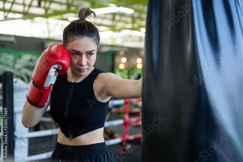 Young woman boxer hitting a huge punching bag at a boxing gym. Female boxer wearing boxing gloves and hitting the punching bag. © somchairakin