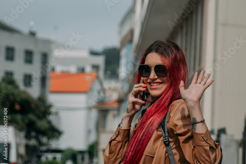 happy young woman with red hair waving and talking on the phone in the street