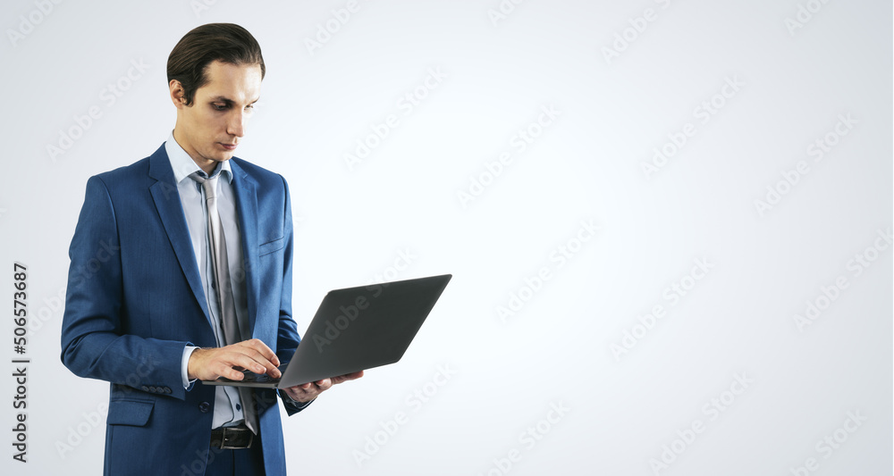 Young businessman in blue suit working with modern laptop, isolated on light grey wall background, with empty space for you text or logo, mockup