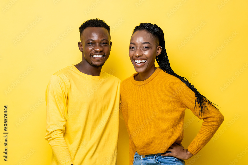 Waist up portrait of positive African couple smiling in isolated yellow color studio background Waist up portrait of positive African couple smiling in isolated yellow color studio background