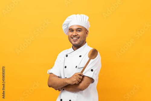Fotografie Young handsome asian man chef in uniform with hat holding ladle utensils cooking in the kitchen various gesture action on isolated yellow background