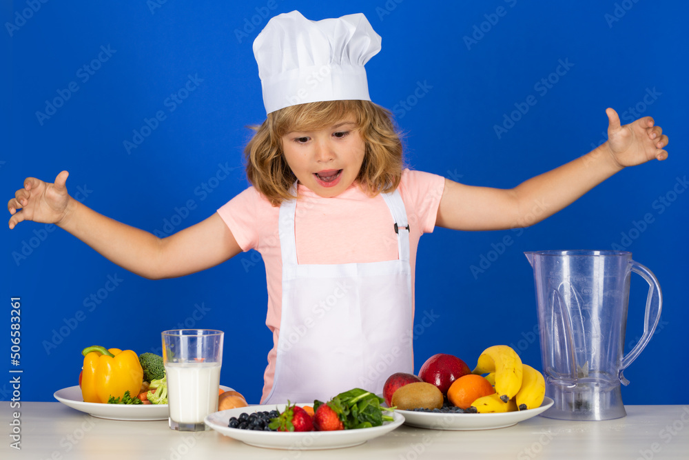 Excited funny chef cook. Fruits and vegetables for kids. Portrait of chef child in cook hat. Cooking at home, kid boy preparing food from vegetable and fruits. Healthy eating. Excited funny chef cook. Fruits and vegetables for kids. Portrait of chef child in cook hat. Cooking at home, kid boy preparing food from vegetable and fruits. Healthy eating.