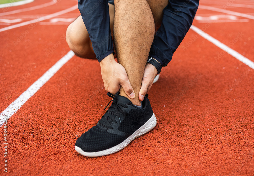 Fototapeta premium Young man runner has sore ankles because he ran too long. Male Exercising until the injury. Overtrained. Young sport man accident running on track