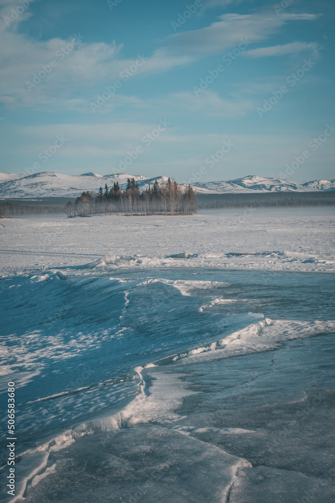 Obraz premium Cracks in the ice of Lake Storsjö looking onto Storådörren during melting winter times. Crevasse leading towards spruce trees and horizon. Copy space included. Vertical orientation.