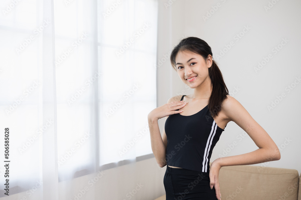 Young beautiful asian woman standing pose smiling to camera. Cheerfully sporty female workout and exercise wearing sport wear at home. Charming woman fitness training and stretching in living room Young beautiful asian woman standing pose smiling to camera. Cheerfully sporty female workout and exercise wearing sport wear at home. Charming woman fitness training and stretching in living room
