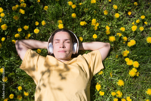 Audio healing. meditation. Slow life. Enjoying the little things. Dreaming of spring. middle aged woman wearing headphones listens to music lying on the grass with dandelions on a spring day. burnout  photo