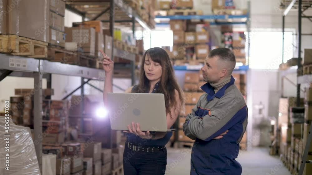 Supervisor together with worker using laptop check goods on shelves of large distribution center for cargo delivery. Distribution, Logistics. Employees carry out inventory in warehouse using computer Supervisor together with worker using laptop check goods on shelves of large distribution center for cargo delivery. Distribution, Logistics. Employees carry out inventory in warehouse using computer