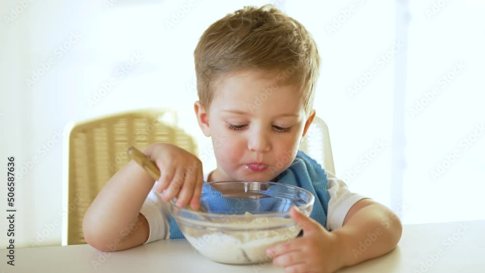 baby eats cereal porridge.Child sits at table and eats porridge.Family breakfast in kitchen.Child at table in kindergarten.Child proper nutrition.Breakfast in kindergarten.Happy dirty child with spoon baby eats cereal porridge.Child sits at table and eats porridge.Family breakfast in kitchen.Child at table in kindergarten.Child proper nutrition.Breakfast in kindergarten.Happy dirty child with spoon