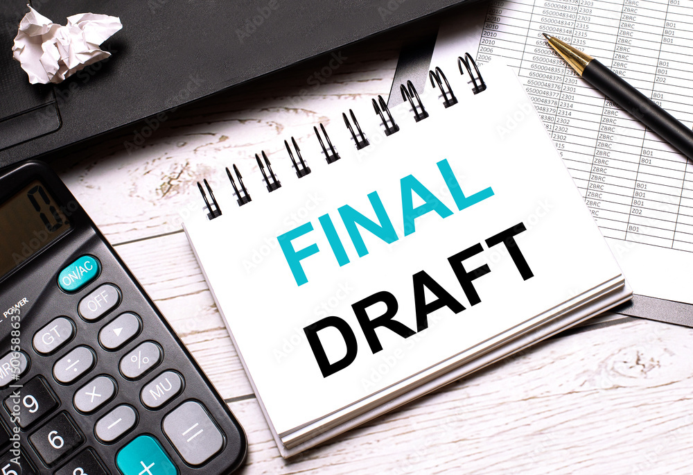 On a light-colored office table is a computer, a black calculator, a pen, and a notebook with the text FINAL DRAFT. Business concept. On a light-colored office table is a computer, a black calculator, a pen, and a notebook with the text FINAL DRAFT. Business concept.