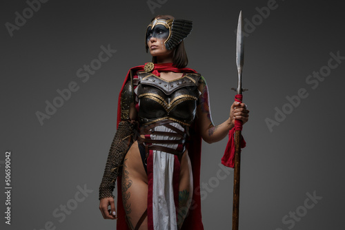 Fotografie, Obraz Studio shot of wild female warrior from past with painted face holding spear isolated on grey background