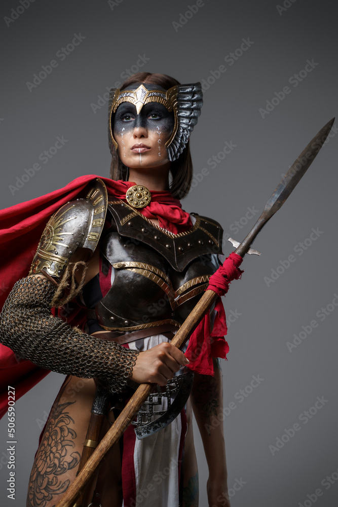 Fototapeta premium Shot of female ancient fighter with red cloak and brown hairs holding spear.
