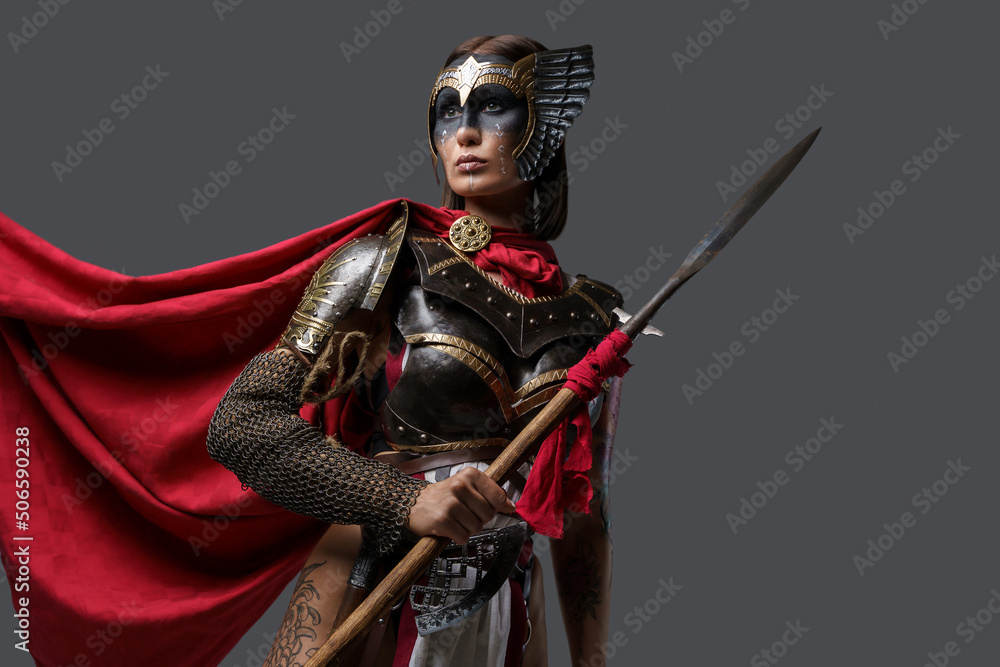 Fototapeta premium Shot of female ancient fighter with red cloak and brown hairs holding spear.