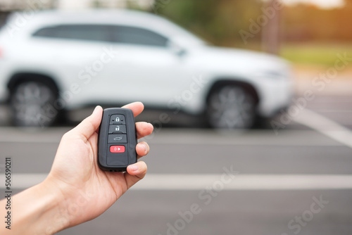 Hand holding car remote control, smart key to lock or unlock doors of white car. Safety, travel and transportation concept