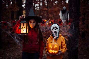 Children in halloween costumes with pumpkin in dark spooky forest. Small boy in mask of a ghost, girl holding lantern