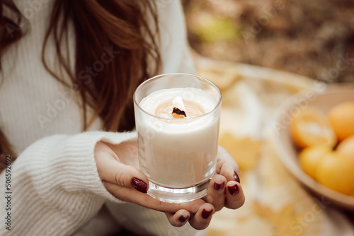 Woman holding burning candle in hands outdoors. Having picnic, relax outdoors in autumn park