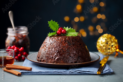 Christmas pudding, fruit cake. Traditional festive dessert. Dark background with lights garland. Close up.