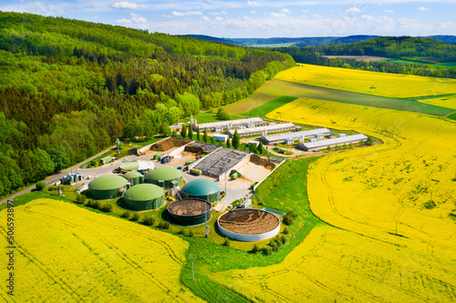 Biogas plant and farm in blooming rapeseed fields. Renewable energy from biomass. Aerial view to modern agriculture in Czech Republic and European Union.	