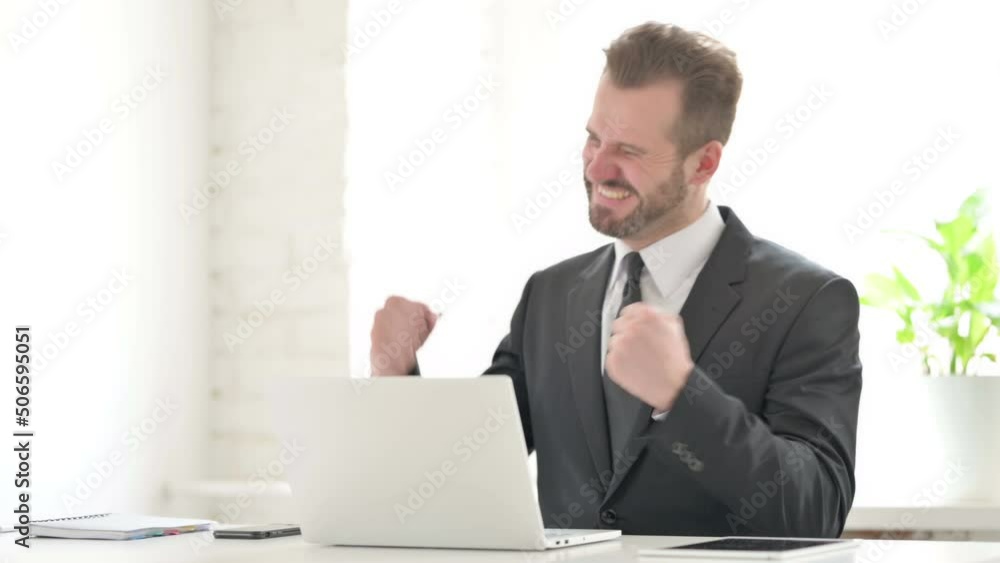 Young Businessman Celebrating Success while using Laptop in Office Young Businessman Celebrating Success while using Laptop in Office