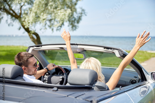 road trip, travel and tourism concept - happy couple driving in convertible car
