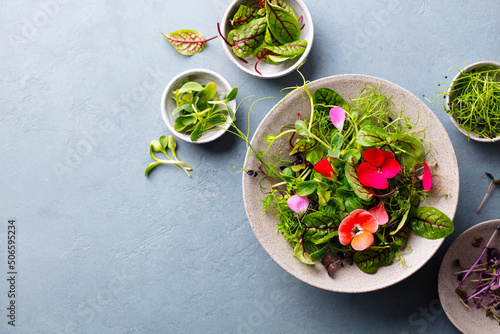 Green salad leaves with edible flowers in bowl. Grey background. Copy space. Top view.