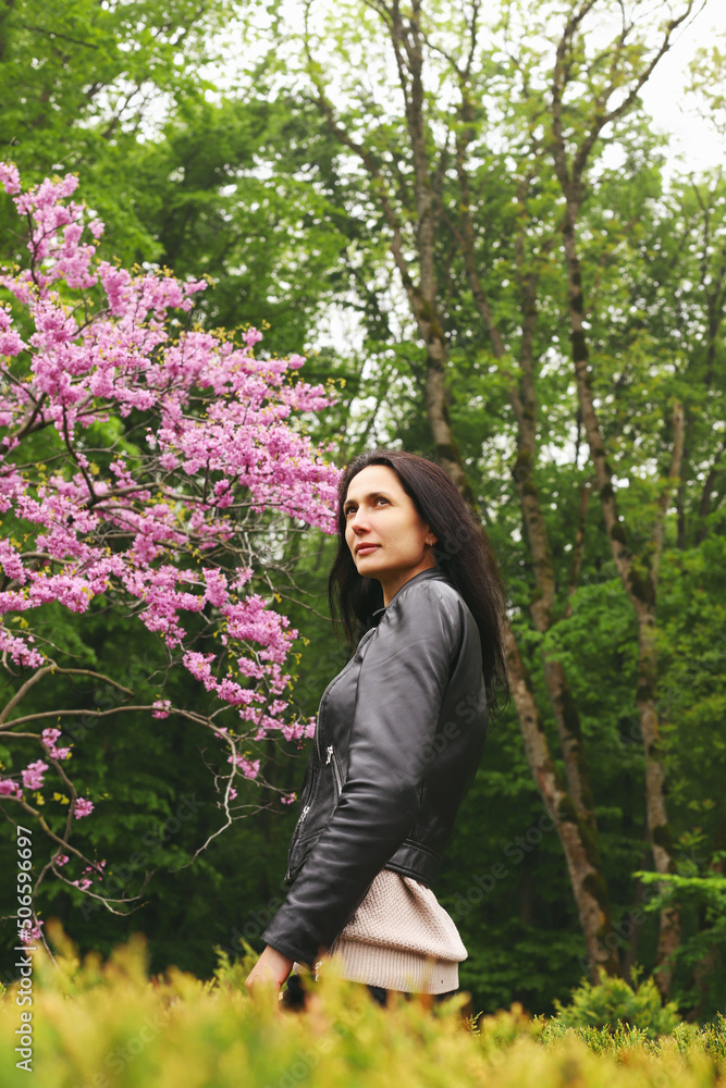 A girl poses on the street near a flowering tree.