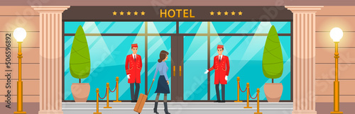 Doormen in red uniform next to door inviting to hotel. Girl with suitcase near entrance to building. Main front entrance to luxury hotel. Staff and guest of establishment near large building