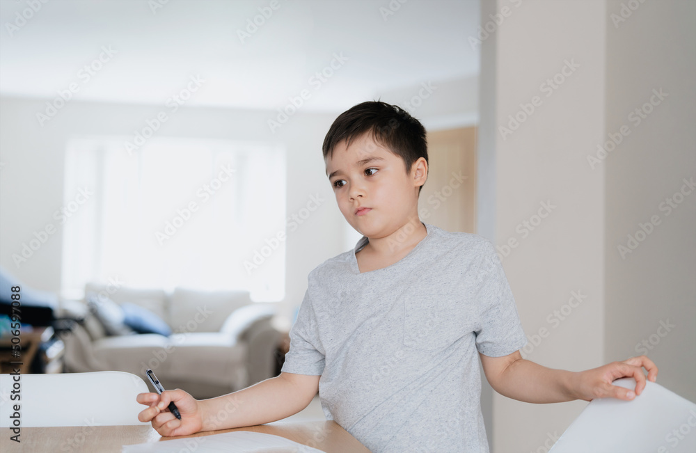 Portrait Young boy holding black pen looking deep in thought, School Kid looking out with thinking face. School kid doing homework, Child with curious face standing alone in lving room Portrait Young boy holding black pen looking deep in thought, School Kid looking out with thinking face. School kid doing homework, Child with curious face standing alone in lving room