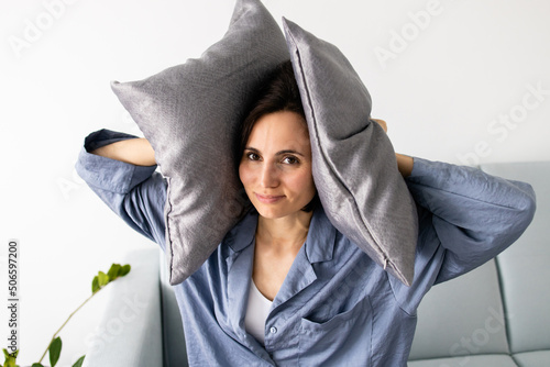 Close up of woman's face covering her ears with a pillows who is frustrated by noise of neighbors. Concept of insomnia, stress and tinnitus