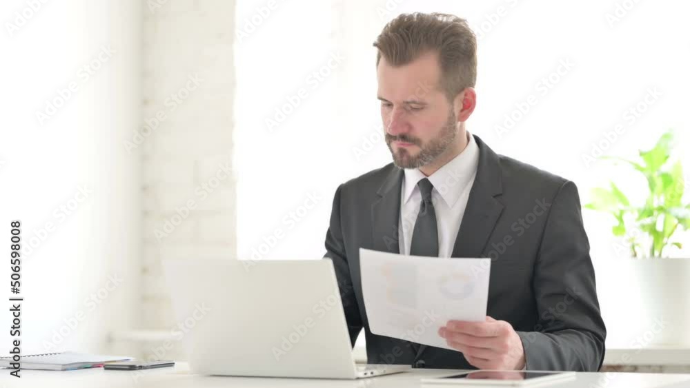Young Businessman with Laptop Having Loss while Reading Documents Young Businessman with Laptop Having Loss while Reading Documents