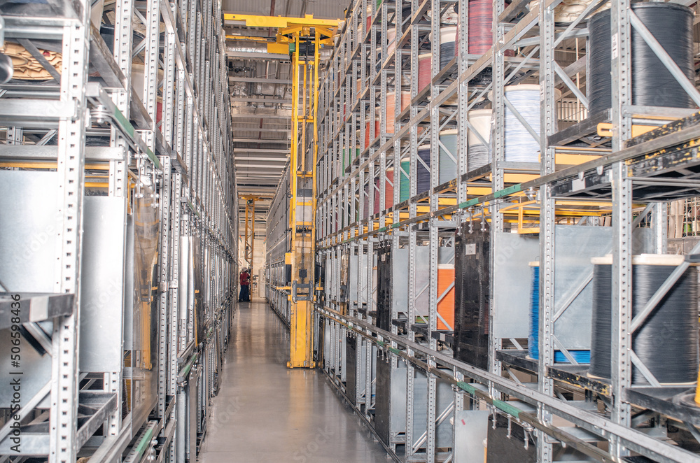 Interior of a modern storage warehouse with coils of colored cable on metal shelves. Forklift lift at the factory. Interior of a modern storage warehouse with coils of colored cable on metal shelves. Forklift lift at the factory.