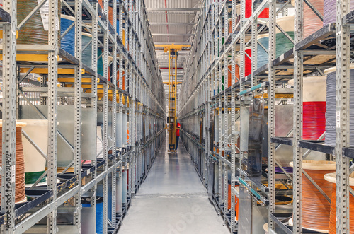 Interior of a modern storage warehouse with coils of colored cable on metal shelves. Forklift lift at the factory.