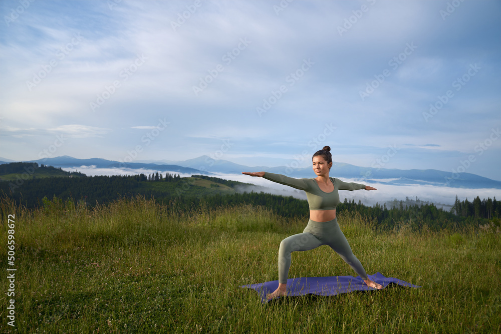 Active female person in sport outfit doing yoga exercises outdoors. Young woman spending summer day on fresh air for intense workout. 