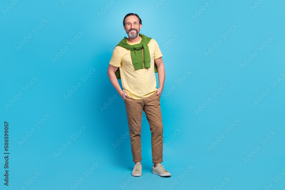 Full size portrait of confident cheerful person hands pockets toothy smile isolated on blue color background Full size portrait of confident cheerful person hands pockets toothy smile isolated on blue color background