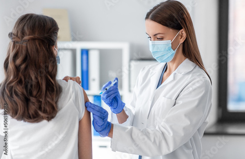 health, medicine and pandemic concept - female doctor or nurse wearing protective medical mask and gloves with syringe vaccinating patient at hospital