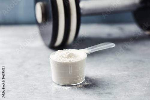 Scoop of Whey Protein and a dumbbell. Bodybuilding food supplements on stone background. Soft focus. Close up. Copy space. photo