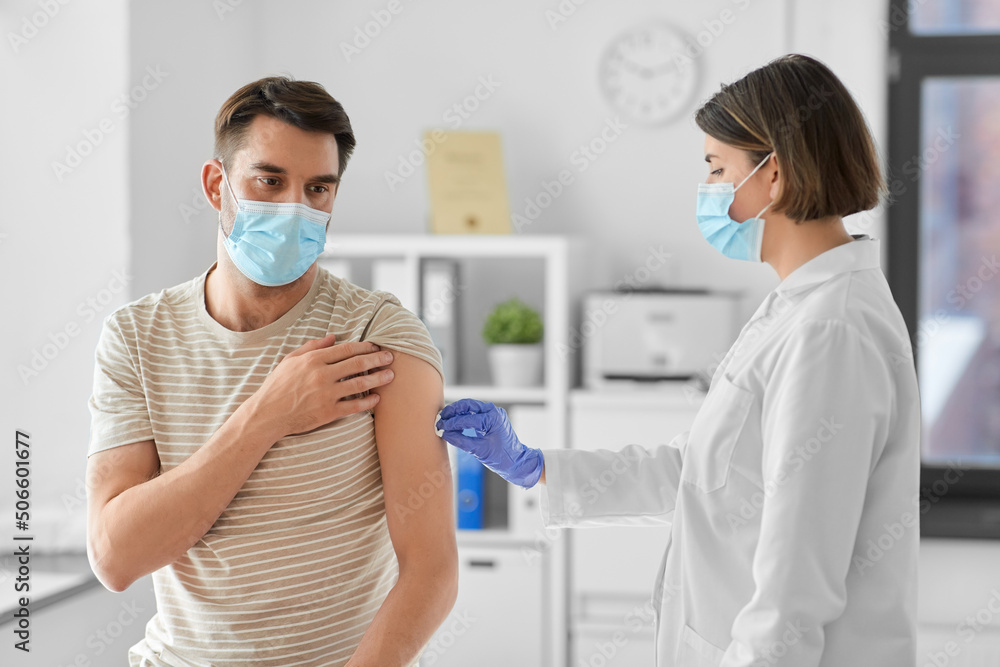 health, medicine and pandemic concept - female doctor or nurse in protective medical mask and gloves disinfecting male patient's skin at hospital
