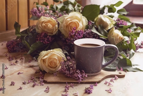 Bouquet of purple lilacs with yellow roses. Gray cup of coffee. Romantic spring flowers. Top view on window background.