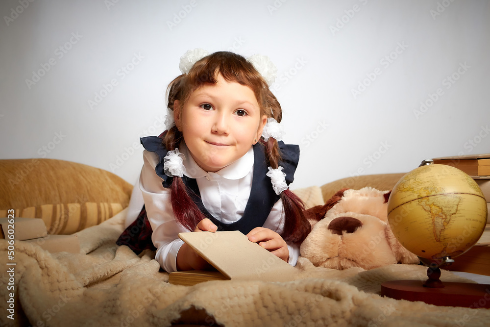 A pretty little girl with book with ponytails and bows in a school uniform having rest on a festive day of study in Russia on September 1. Photo shoot with a young student A pretty little girl with book with ponytails and bows in a school uniform having rest on a festive day of study in Russia on September 1. Photo shoot with a young student