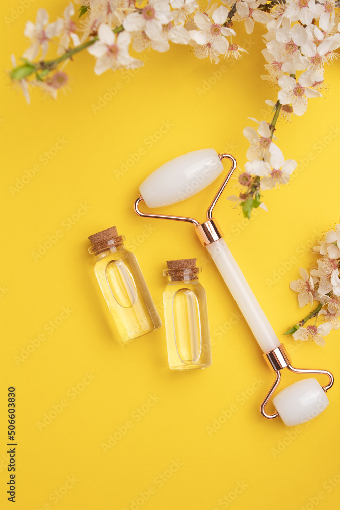 Glass bottles with oil, face roller for face massage on a yellow background with blooming cherry. Cosmetic facial skin care and spa. Natural treatment concept. Glass bottles with oil, face roller for face massage on a yellow background with blooming cherry. Cosmetic facial skin care and spa. Natural treatment concept.
