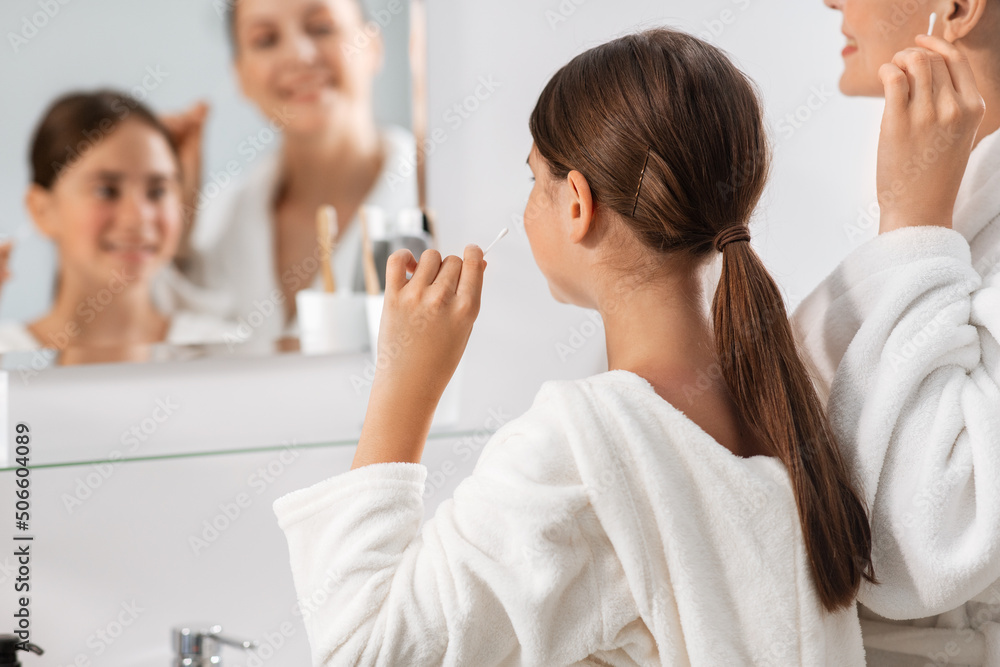 beauty, hygiene, morning and people concept - happy smiling mother and daughter cleaning ears with cotton swabs and looking to mirror at bathroom beauty, hygiene, morning and people concept - happy smiling mother and daughter cleaning ears with cotton swabs and looking to mirror at bathroom