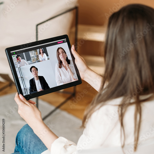 Video interview. Digital meeting. Online communication. Female executive watching diverse business team working online discussing project on tablet screen at home virtual office. © golubovy