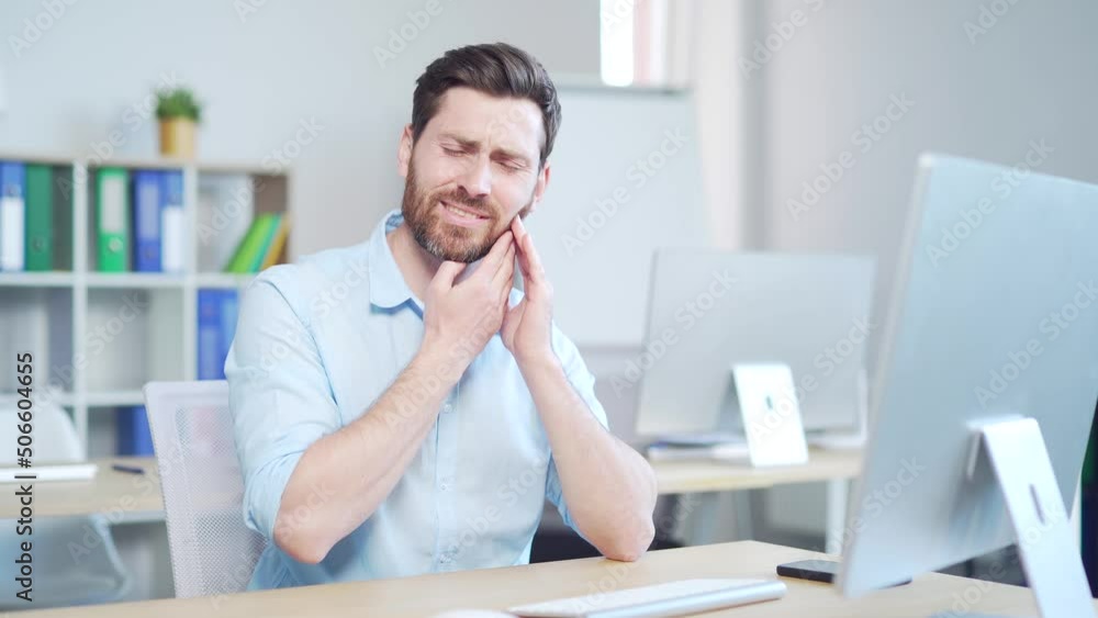 Young handsome bearded caucasian man employee with severe toothache. male worker indoors suffers from Strong pain. Sitting at work in workplace office. painful expression dental illness on teeth Young handsome bearded caucasian man employee with severe toothache. male worker indoors suffers from Strong pain. Sitting at work in workplace office. painful expression dental illness on teeth