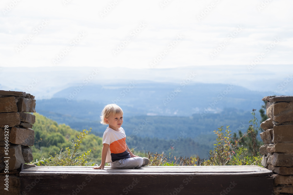 Fototapeta premium rear view blonde kid boy sitting outdoors on the bench and enjoying beautiful nature view