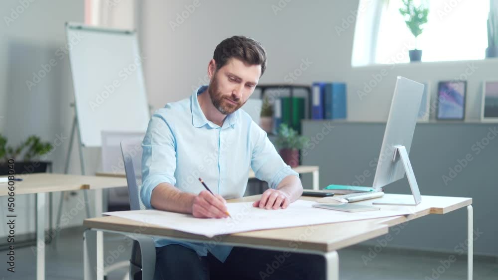 young creative designer or architect working in the office at work at a computer desk with drawings. Handsome man doing project work sitting at workplace indoors sketching a housing plan building young creative designer or architect working in the office at work at a computer desk with drawings. Handsome man doing project work sitting at workplace indoors sketching a housing plan building