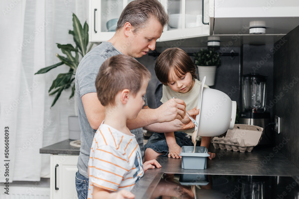 Caring dad is cooking in the kitchen with his two sons. Boys and dad prepare pie dough, muffins, pancakes for breakfast at home. Family time together Caring dad is cooking in the kitchen with his two sons. Boys and dad prepare pie dough, muffins, pancakes for breakfast at home. Family time together