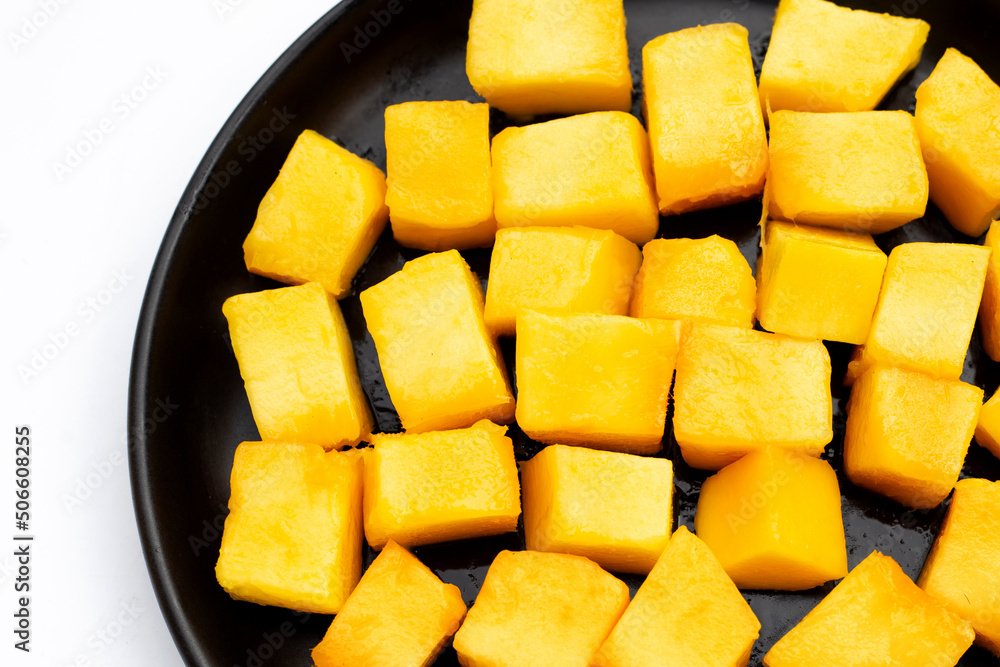 Yellow mango cube slices in black plate on white background. Yellow mango cube slices in black plate on white background.