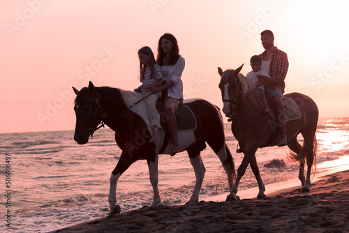 The family spends time with their children while riding horses together on a sandy beach. Selective focus 