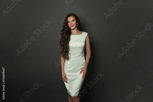 Brunette female model with long healthy shiny wavy hairstyle. Beautiful young woman with curly hair in silky dress smiling © millaf
