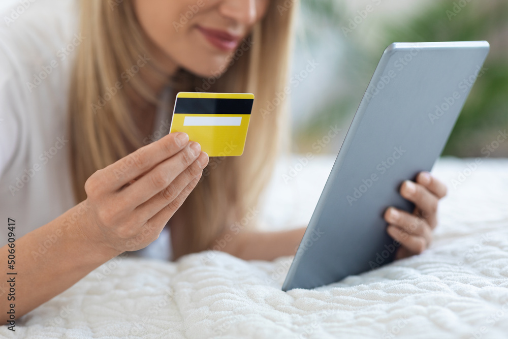 Unrecognizable woman laying in bed with tablet and credit card Unrecognizable woman laying in bed with tablet and credit card