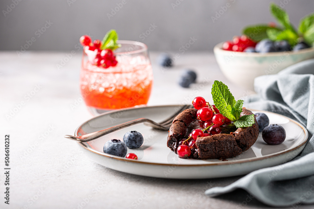 Warm chocolate Lava Cake with bite taken out of molten center, red currants, bleuberry and mint leaves on gray background Warm chocolate Lava Cake with bite taken out of molten center, red currants, bleuberry and mint leaves on gray background